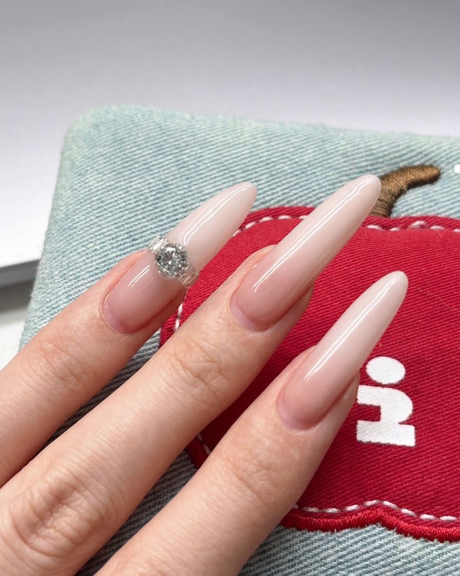 Eine Nahaufnahme zeigt einen Nagelpinsel, der weiße Gel-Pigmente auf die Spitze eines langen Nude-Stiletto-Nagels aufträgt.