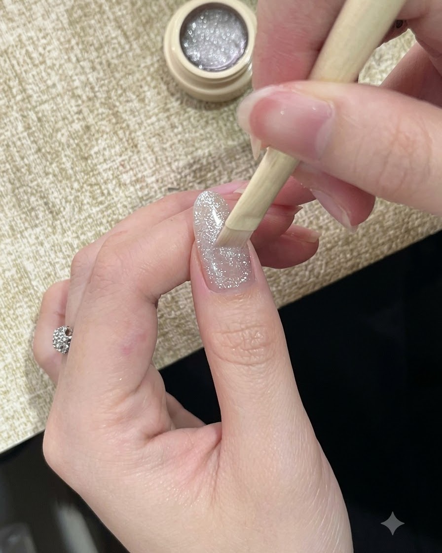 Ein Pinsel trägt einen hochreflektierenden, glitzernden silbernen Cat-Eye-Gellack auf einen Fingernagel auf.