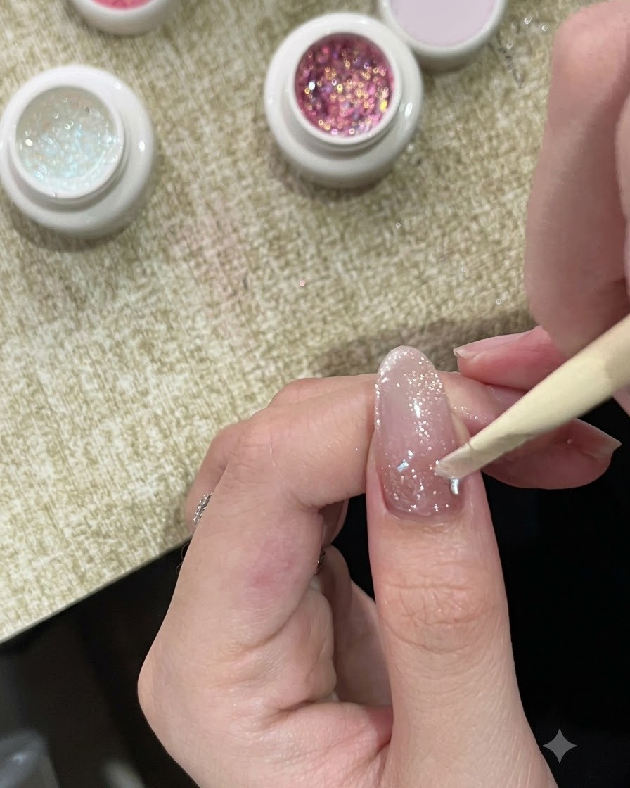 Ein Rosenholzstäbchen platziert klobigen, schimmernden Bubble-Glitter im Nagelhautbereich eines lackierten Nagels.