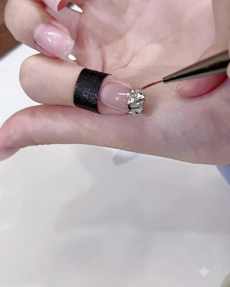 Ein dünner Nail Art Pinsel trägt klaren Strasssteinkleber präzise um die Ränder eines Strassstein-Musters auf einem lackierten Fingernagel auf.