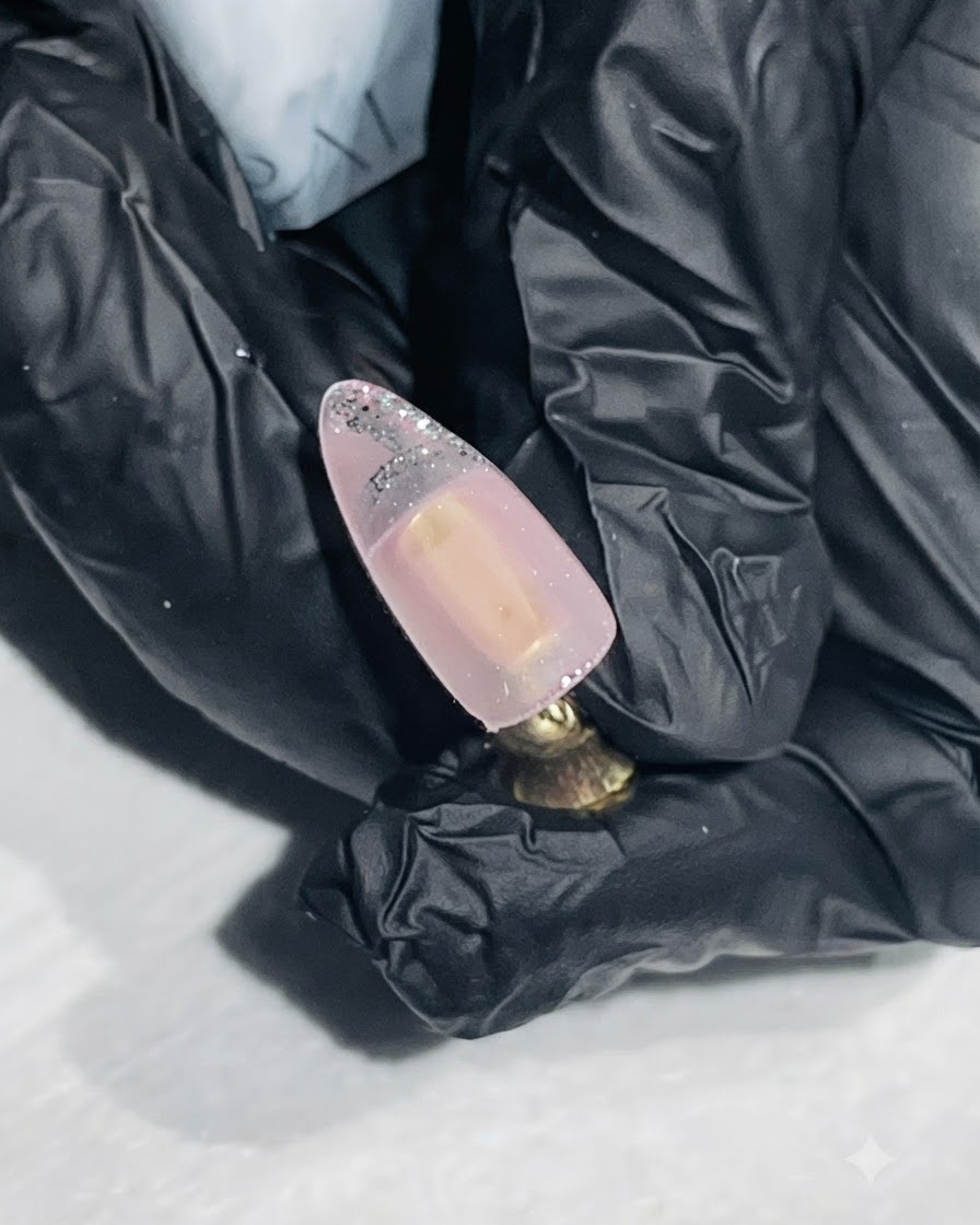 Ein feiner Liner-Pinsel zieht eine silberne Kontur auf die Spitze eines Nude-farbenen Nagels.