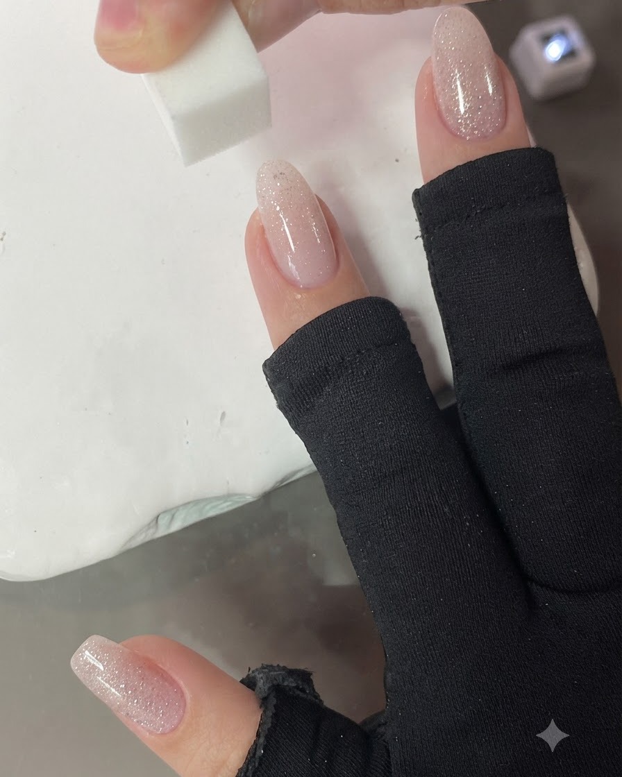 Ein kleiner Make-up-Schwamm tupft vertikal auf den Nagel, um den Nude-Rosa-Verlauf zu verblenden.