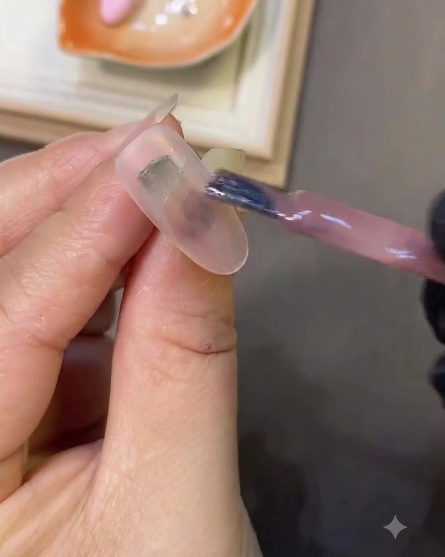 Ein Nagelpinsel trägt hellrosa Cat-Eye-Gel auf einen milchweißen Nagel auf.