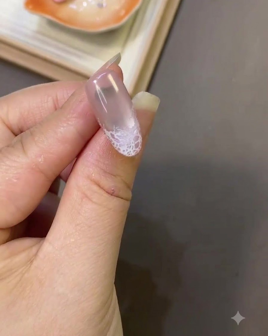 Eine Nahaufnahme eines Fingernagels mit einem fertigen weißen Spitzendesign in der Nähe der Spitze und glatter Oberflächentextur.