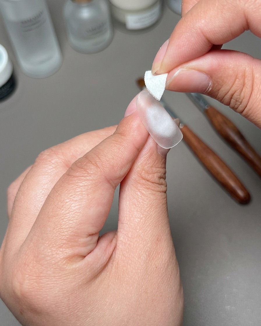 Eine Hand hält einen kleinen weißen Aufkleber über die Mitte einer vorbereiteten Nagelspitze.