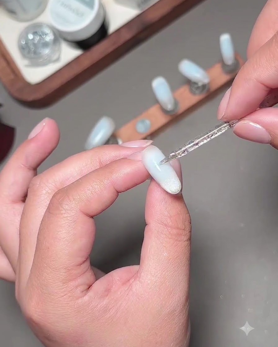 Ein feiner Nagelkunstpinsel trägt eine zweite Schicht blauen Gels auf, um die Nagelmitte abzunkeln.