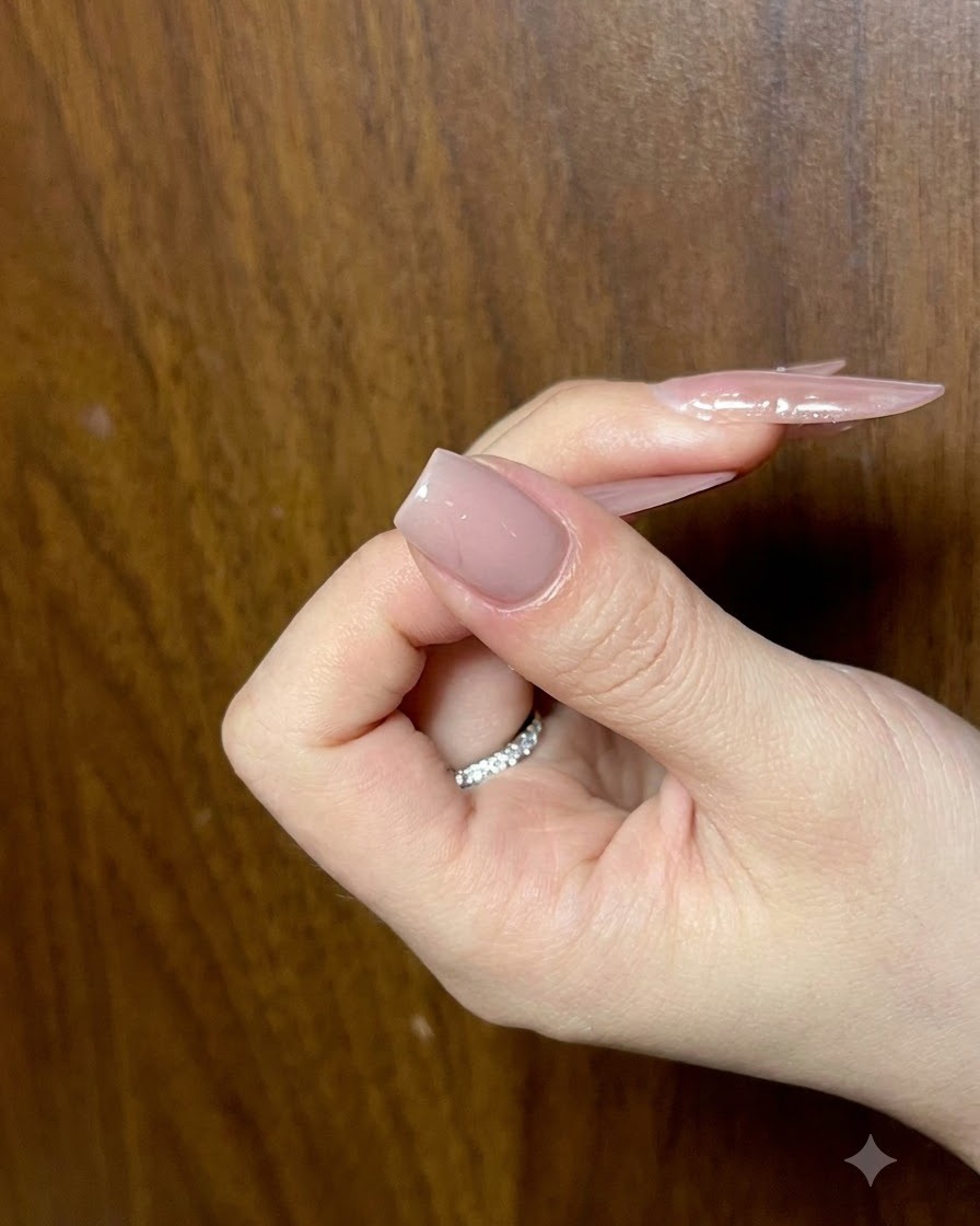 Eine Hand hält einen Nagel mit einer fertigen Nude-Basisschicht, aus einem Winkel fotografiert, um die Glätte zu prüfen.