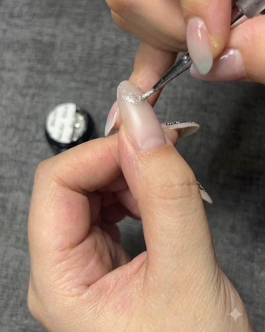 Ein feiner Detailpinsel trägt glitzerndes silbernes Gel auf, um eine Schmetterlingskontur auf einem Nagel zu erstellen.