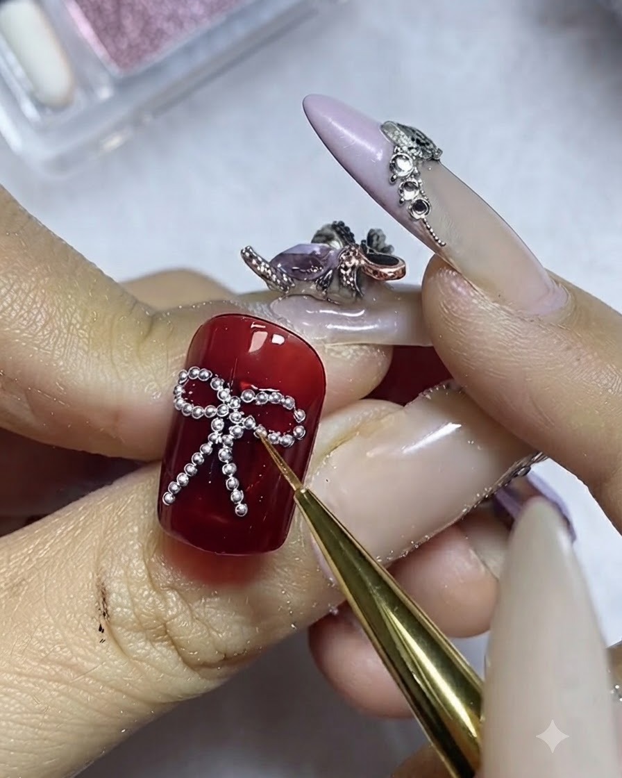 Ein feiner Pinsel trägt Top Coat vorsichtig um den Rand der silbernen Stahlperlen auf einem roten Nagel auf.