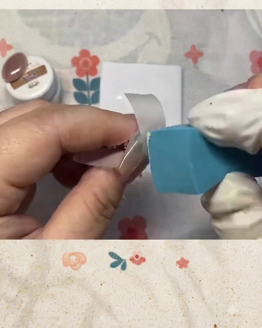 Ein Schwamm tupft sanft weißen Lack auf eine mit Tape abgeklebte Nagelspitze.