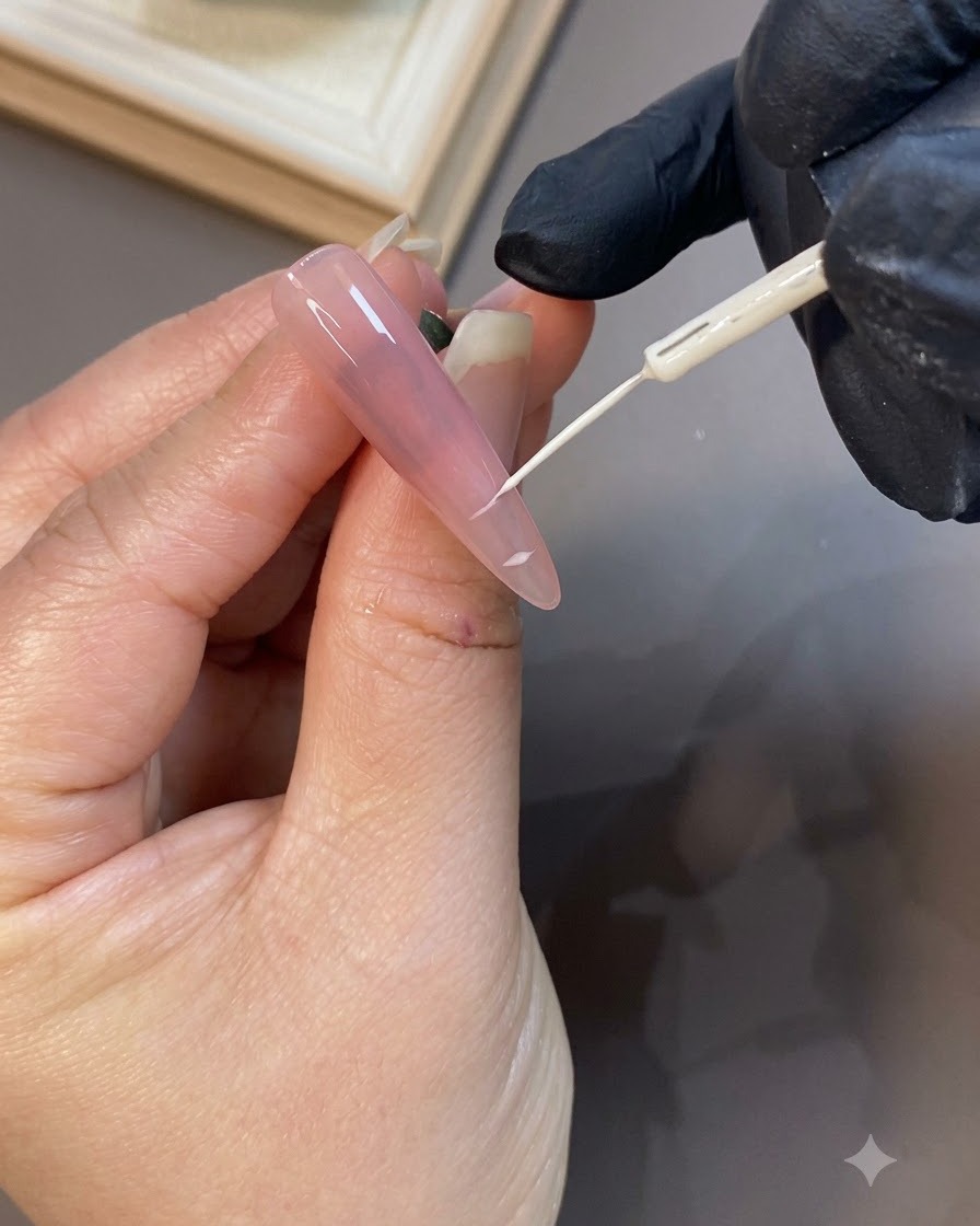 Detailaufnahme eines feinen Nail-Art-Pinsels, der eine weiße French-Tip-Linie auf eine roséfarbene Nagelverlängerung zeichnet.
