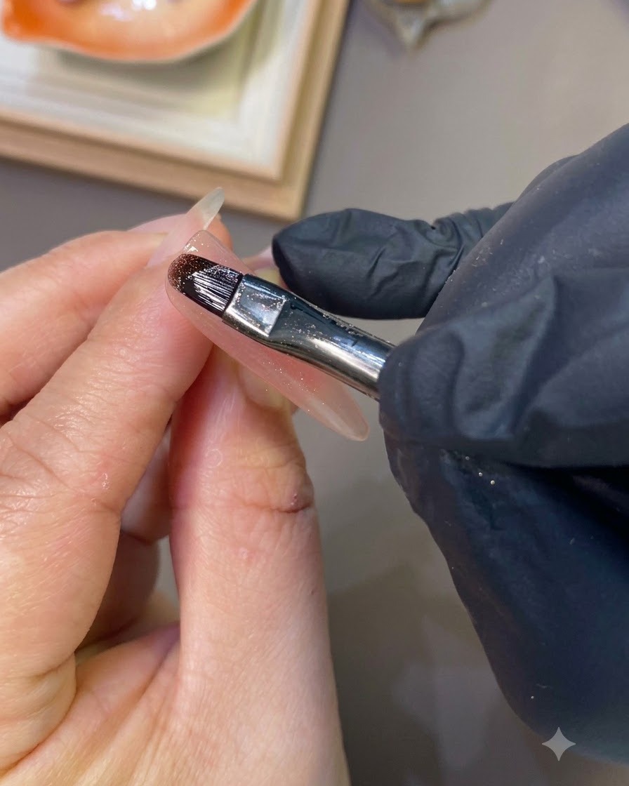 Ein Nagelpinsel, der einen klaren Base Coat auf einen langen, geformten Ringfingernagel aufträgt.