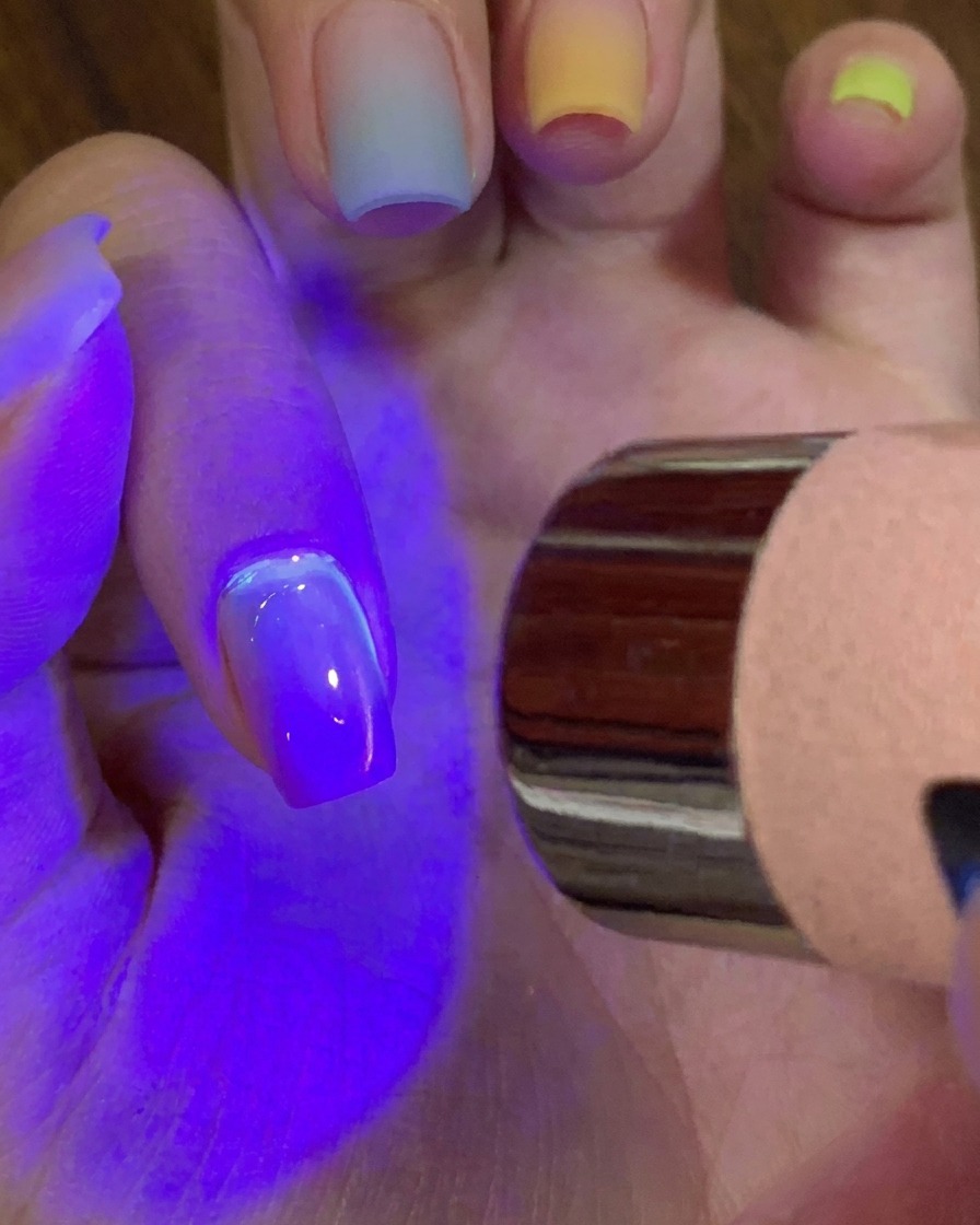 Eine Hand härtet unter einer lila UV-/LED-Lampe mit einem Mini-Taschenlampengerät aus.