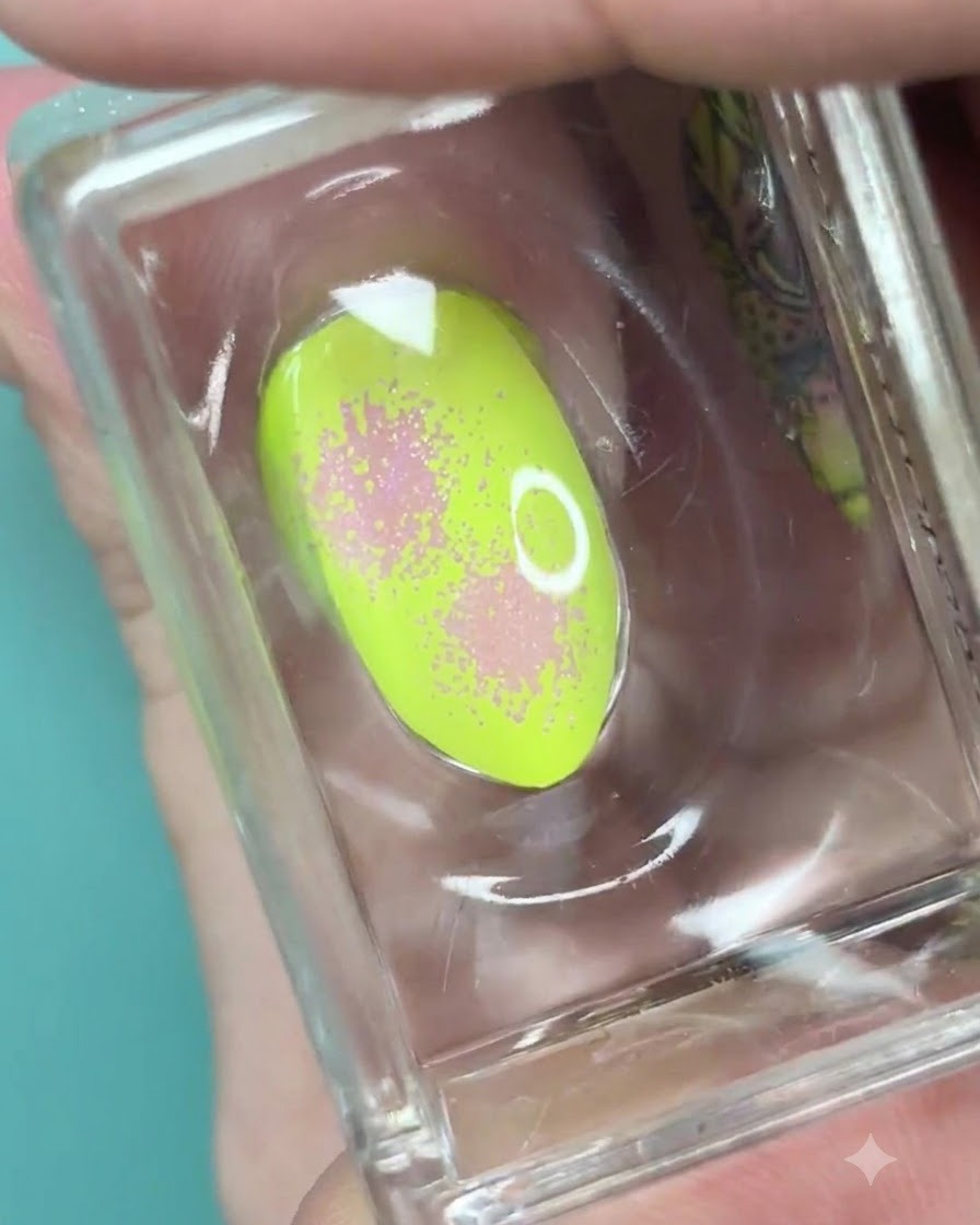 Ein klarer Silikonstempel hält einen neongrünen Nagel mit weichem Pink-Verlauf und punktierter Textur.