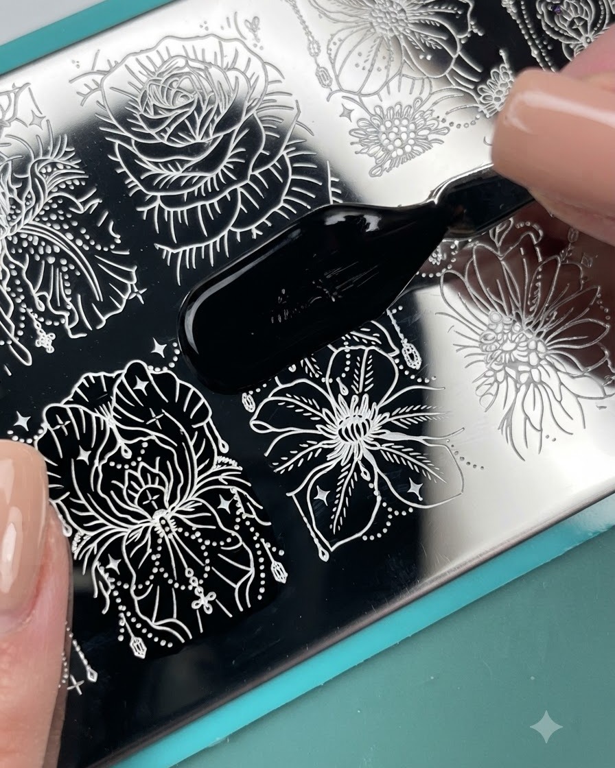 Ein Pinselapplikator trägt schwarzen Stempellack über ein graviertes Blumenmuster auf einer Metall-Stempelplatte auf.