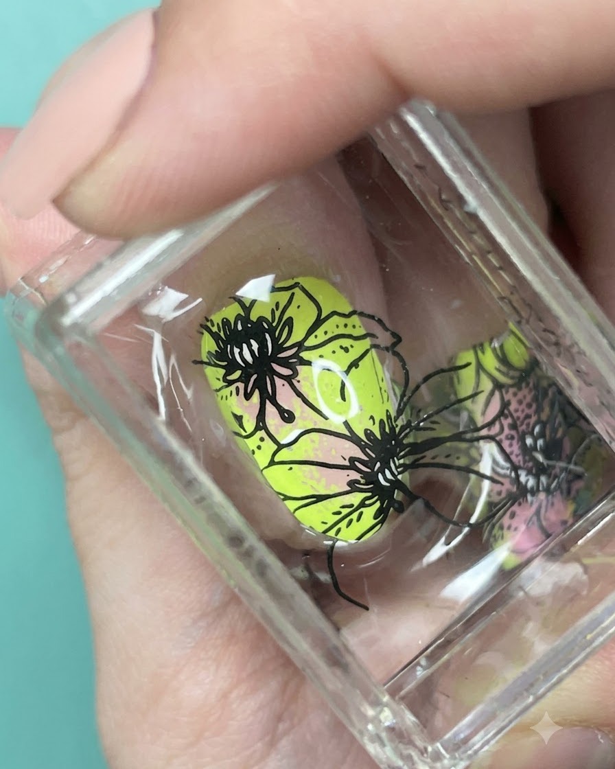 Nahaufnahme von schwarzen Blumenmustern, die auf einem Stempel über dem neongrünen und pinken Ombré-Nagel ausgerichtet sind.