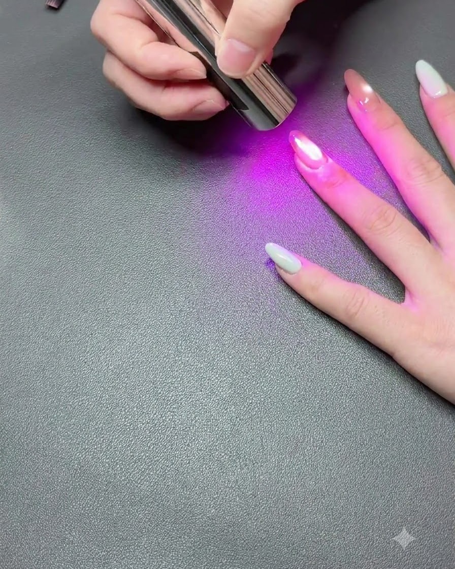 Eine Hand ruht auf einer dunklen Oberfläche, während eine tragbare UV-Lampe das Cat-Eye-Gel-Polish aushärtet.