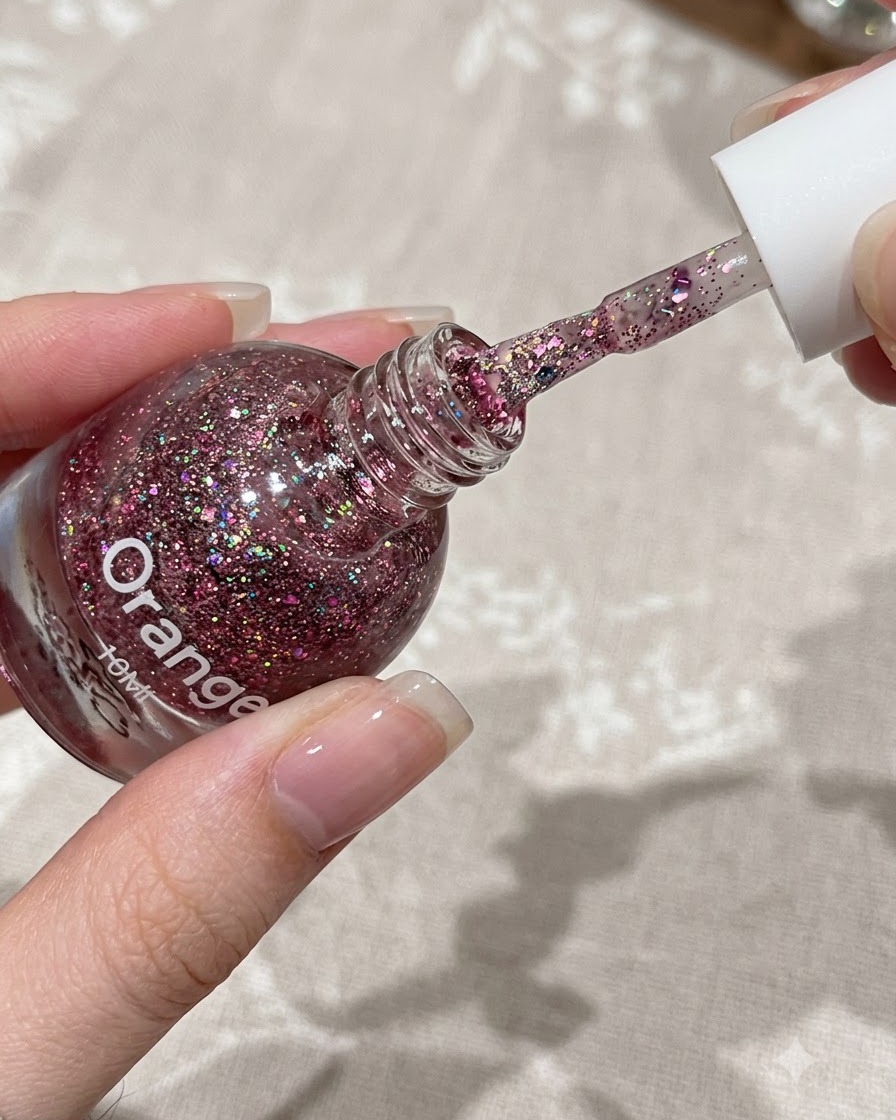 Ein Pinsel trägt eine dünne Schicht pinkes Glittergel auf die obere Hälfte eines natürlichen Fingernagels auf.