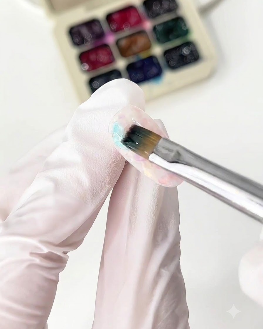 Ein feiner Pinsel trägt blauen Glasgel auf eine Nagelspitze auf.