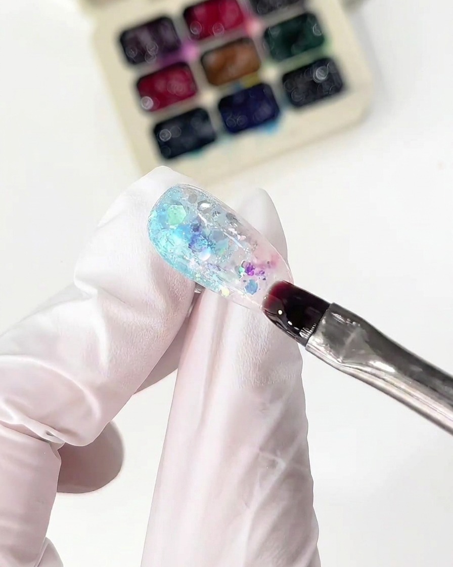 Ein feiner Pinsel trägt rosa Glasgel neben dem blauen Abschnitt auf einem Nagel auf.