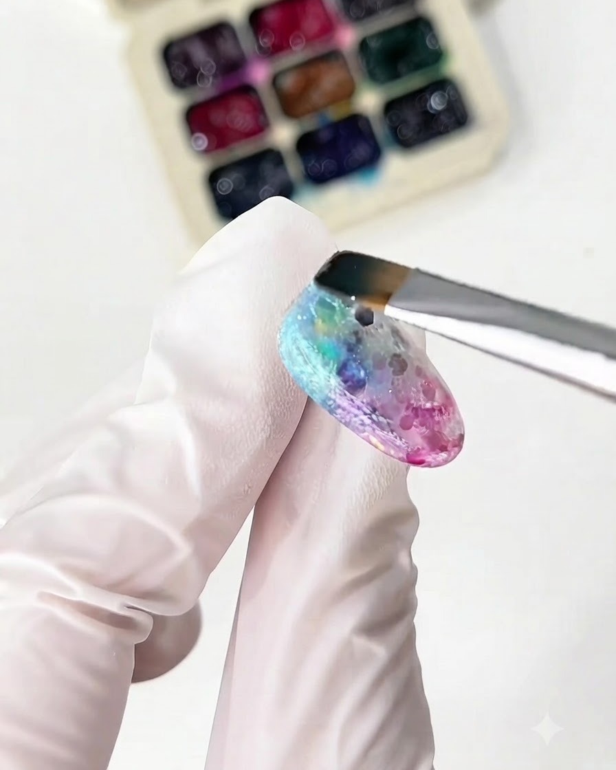 Ein feiner Pinsel trägt gelbes und grünes Glasgel auf den Nagel auf.