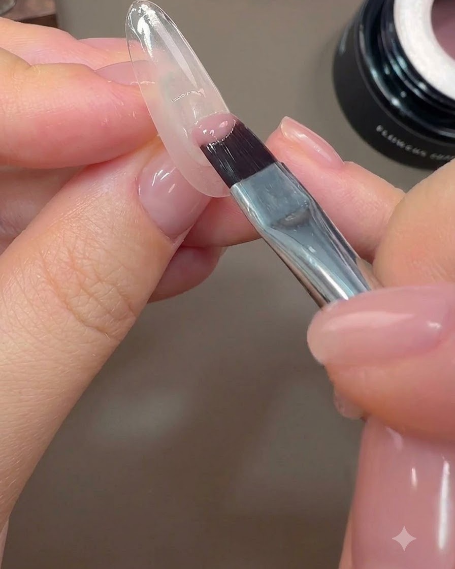 Ein Nagelpinsel trägt eine Halb-Abdeckung aus Nude-Rosa Farbgel auf den hinteren Rand eines Nagels auf.