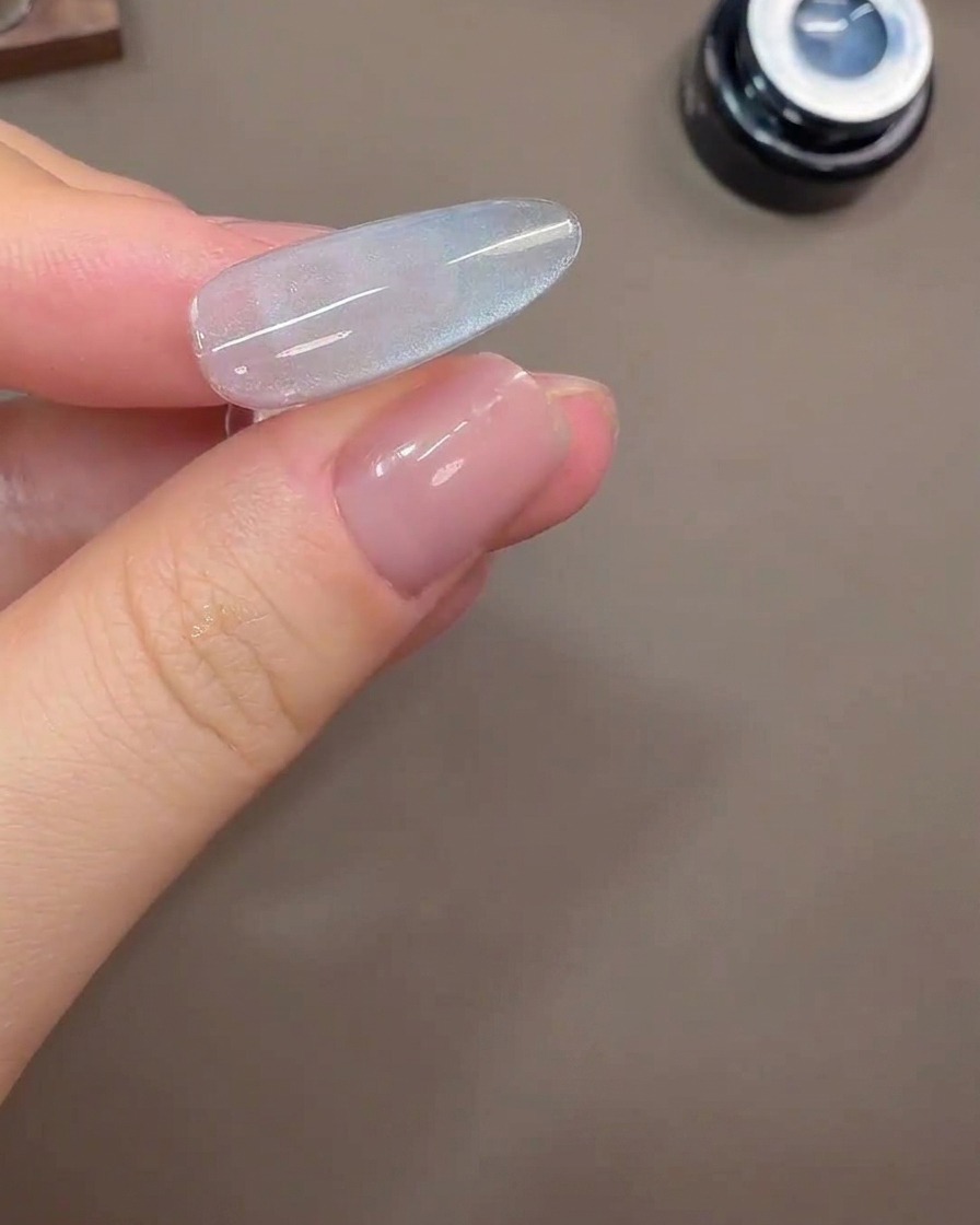 Ein Nagel zeigt eine breite Cat-Eye-Lichtreflexion auf einem grau-blauen Gelhintergrund.