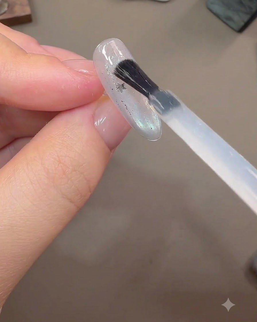Ein Pinsel trägt eine dickere Schicht Aufbaugel über eingebettete Sternen-Glitzerteile auf einer fertigen Nagelverlängerung auf.