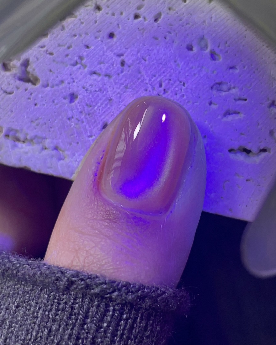 Ein Fingernagel, der unter einer violetten UV/LED-Minilampe aushärtet.