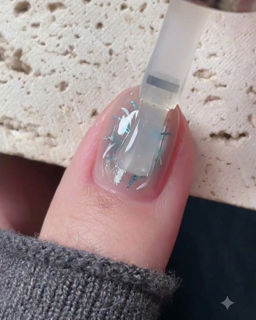 Ein Pinsel trägt einen klaren, selbstnivellierenden Topcoat über ein detailliertes Nagelkunstdesign auf.