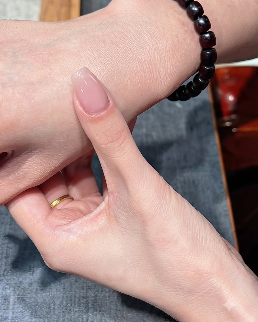 Ein Fingernagel mit einer einzelnen Nude-Schicht wird vor den Handrücken gehalten.