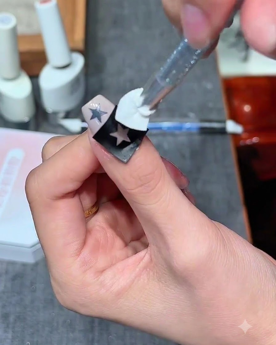 Ein Schwammstempel trägt milchweißes Gel über einem hohlen Sternaufkleber auf einem Nagel auf.