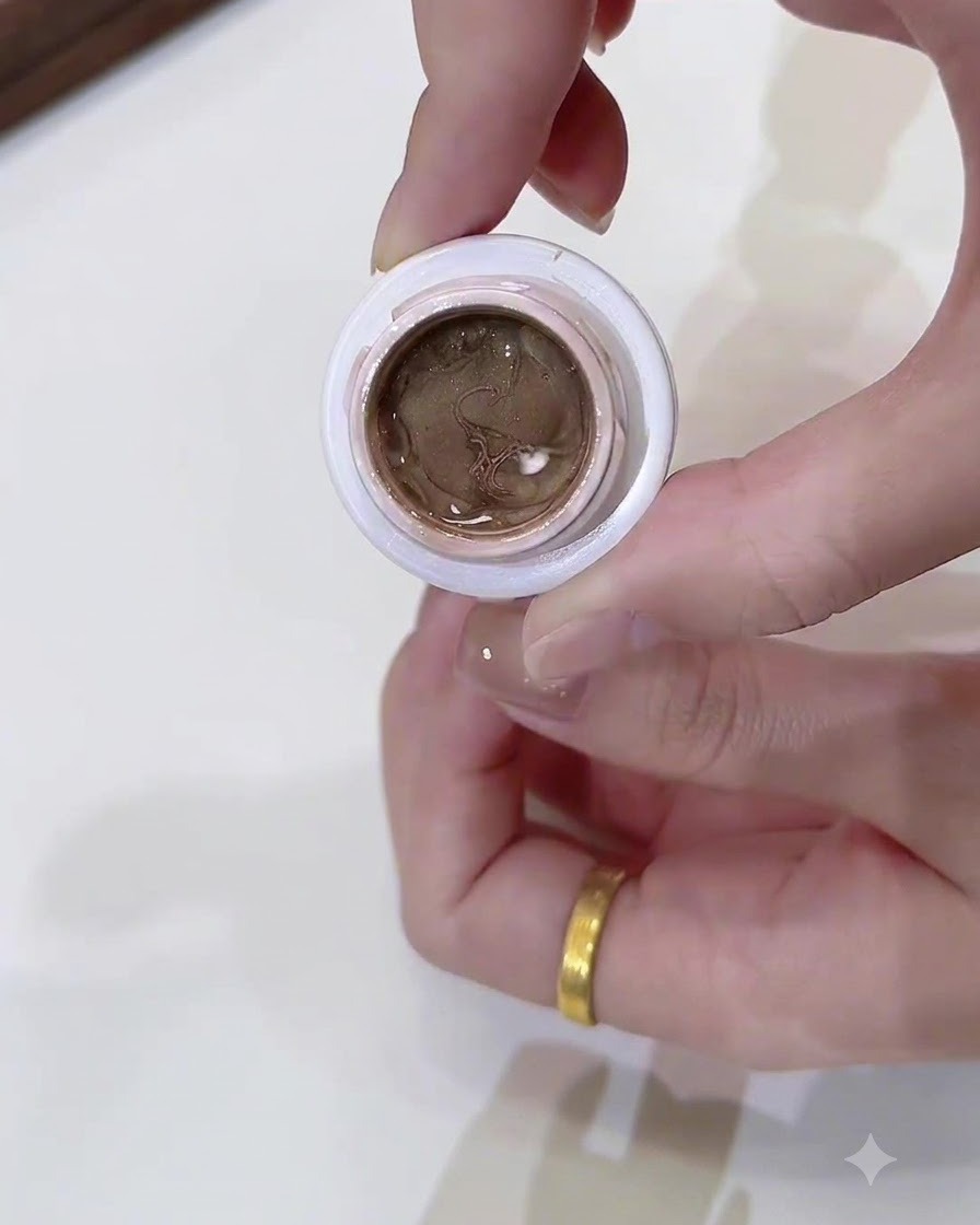 Eine Nahaufnahme eines kleinen, offenen Tiegels gefüllt mit dunklem Champagner-Gold Cat-Eye-Gel, gehalten von einer Hand.