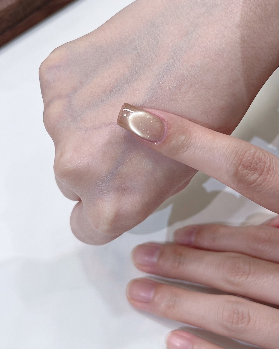 Eine Hand hält einen Magneten, der über einem Champagner-Gold Cat-Eye-Nagel kreist, um einen fließenden Lichteffekt zu erzeugen.