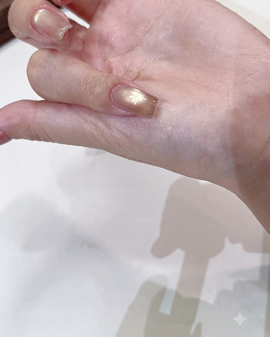 Ein Pinsel trägt einen klaren, glänzenden Topcoat über einen ausgehärteten Champagner-Gold Cat-Eye-Nagel auf.
