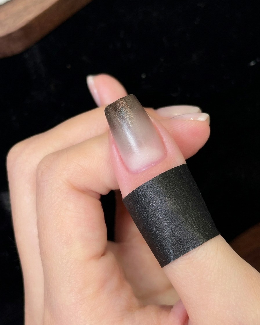 Ein Nagel unter einer kleinen tragbaren UV- und LED-Lampe, der die frisch aufgetragene schwarze Gradientenschicht aushärtet.