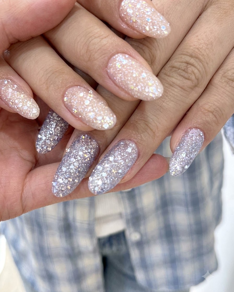 Eine scharfe Makroaufnahme, die feine Glitzerpartikel auf lavendellila Glitter-Gel-Nägeln hervorhebt.
