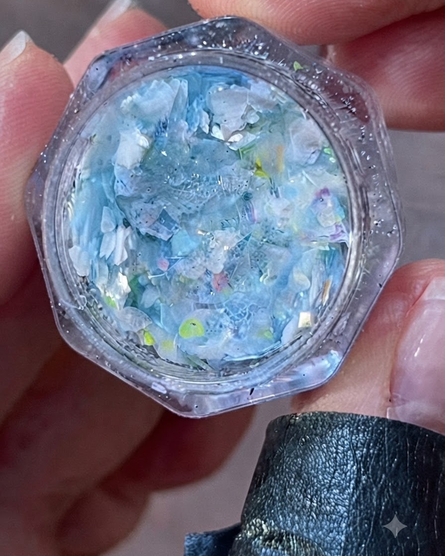 Eine Nahaufnahme eines offenen Glases, gefüllt mit irisierenden blauen und weißen Flocken und Glitter.
