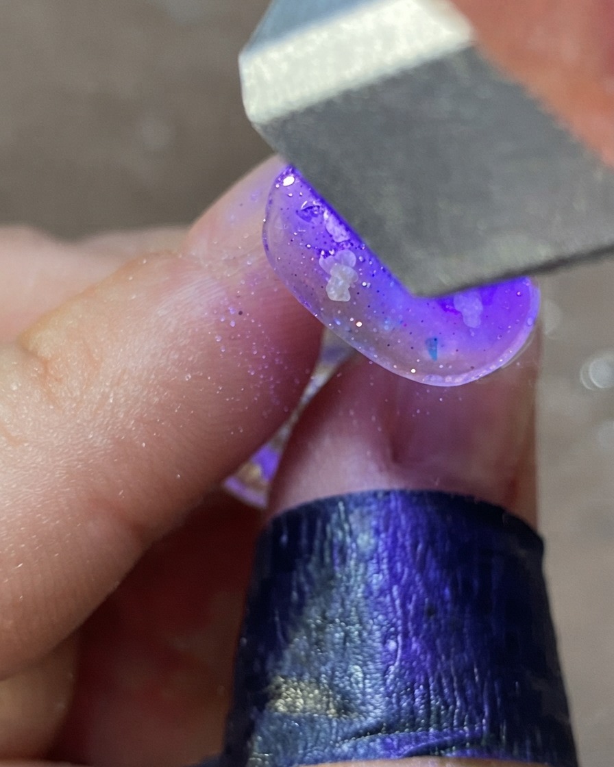 Eine Hand unter einer lila UV/LED-Nagellampe härtet ein verziertes Nageldesign aus.