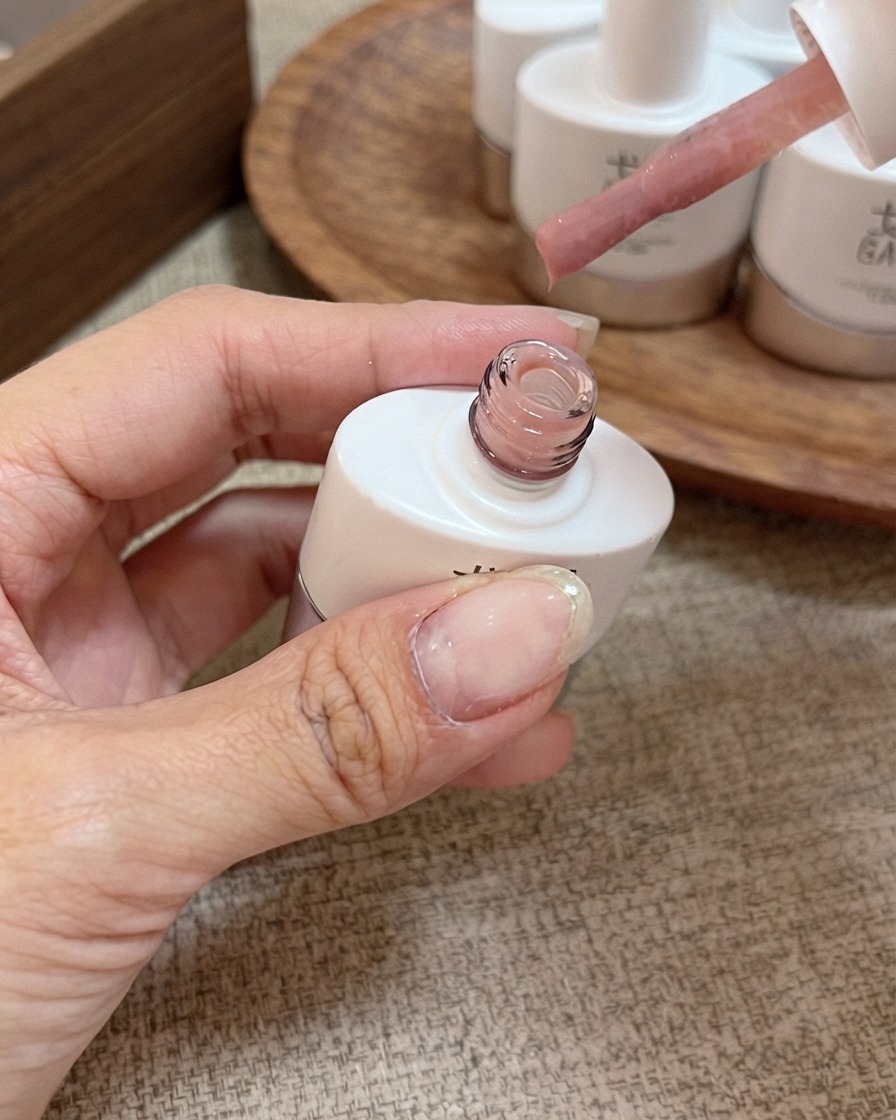Ein Pinselapplikator mit Honey Peach Pink Nude-Gel-Nagellack über einer offenen Flasche.