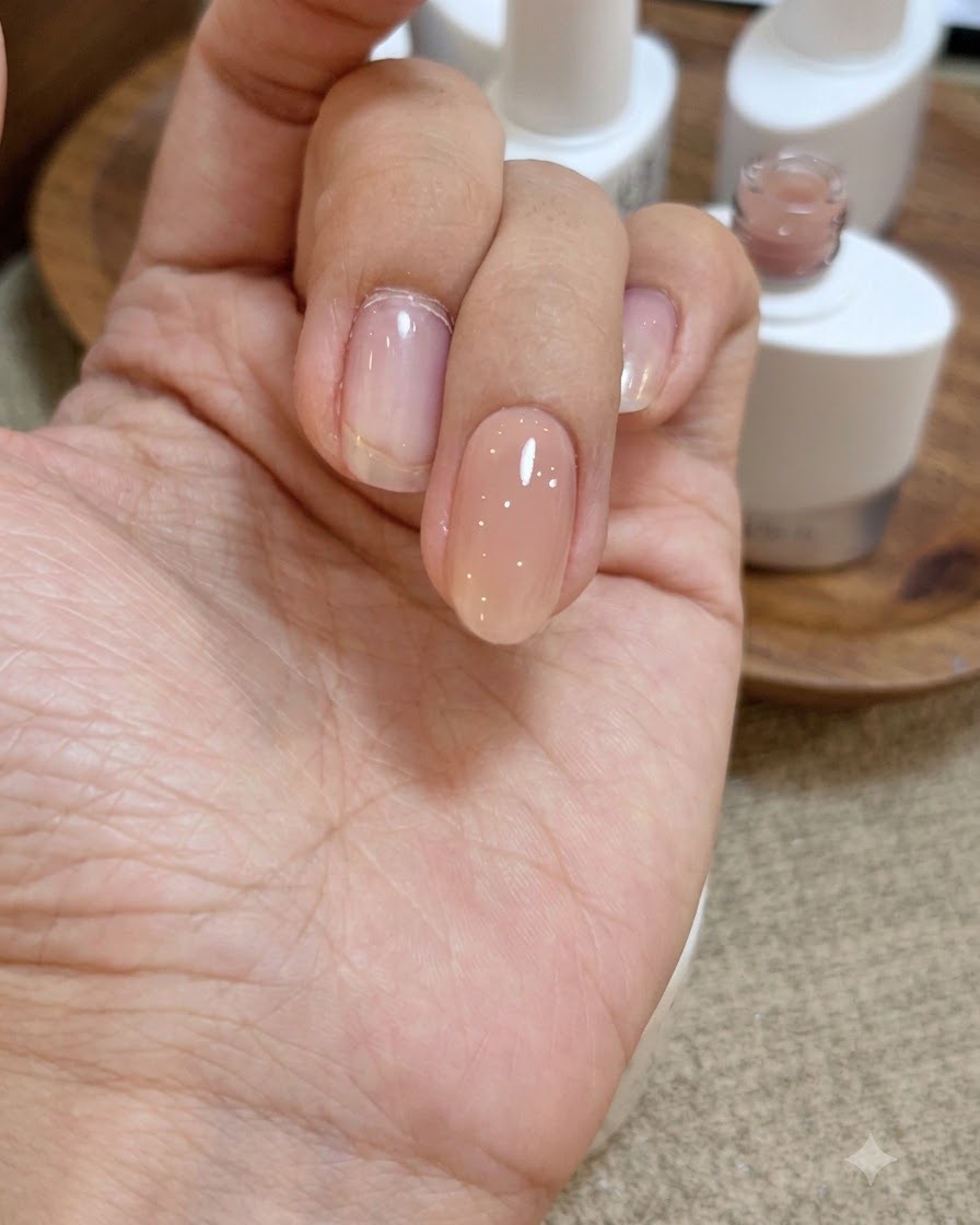 Eine Nahaufnahme einer Hand mit einer nassen, glänzenden Schicht klaren Base-Gels auf dem Nude-Rosa-Nagel.