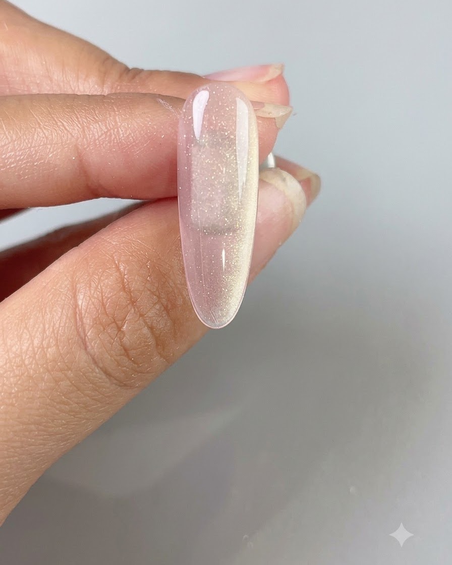 Eine Hand hält einen Magnetstab über einen pinken translucenten Cat-Eye-Gel-Nagel, um einen breiten, leuchtenden Lichtstrahl zu erzeugen.