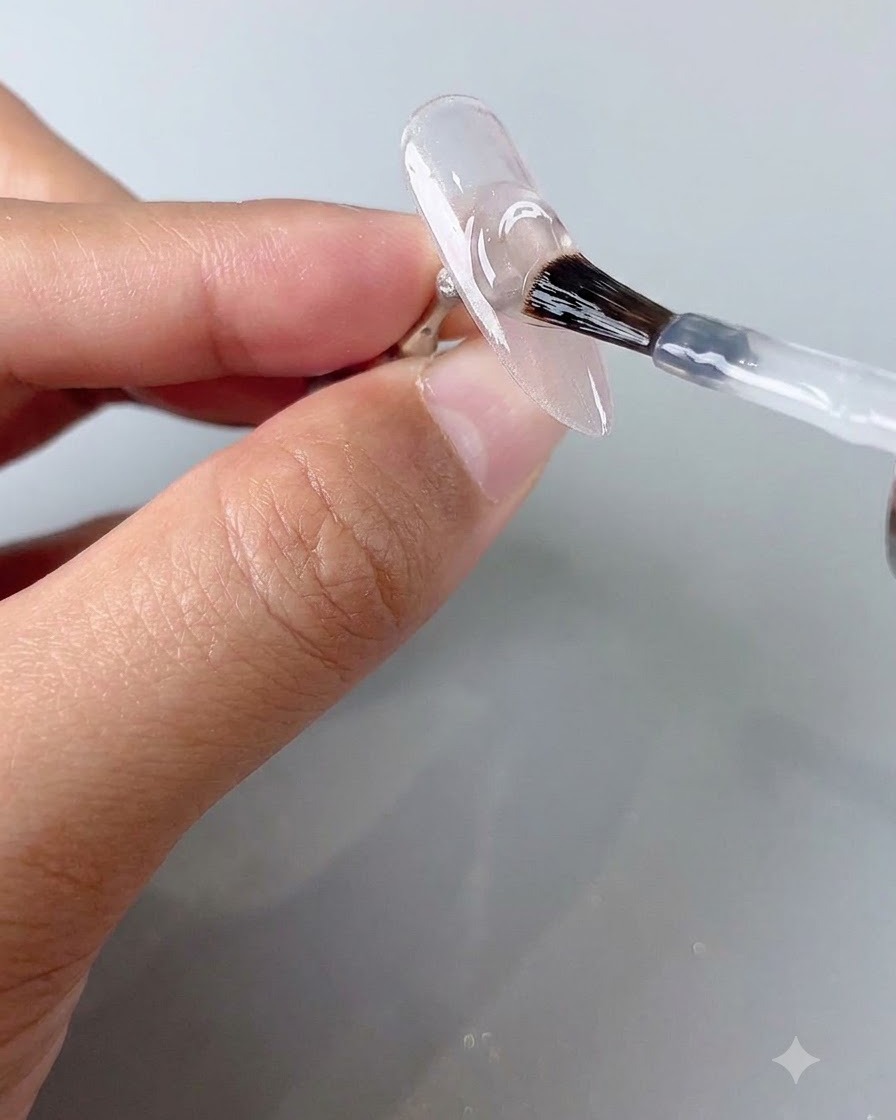 Ein Nagelpinsel trägt eine Schicht klaren Topcoats auf einen ausgehärteten Cat-Eye-Nagel auf.