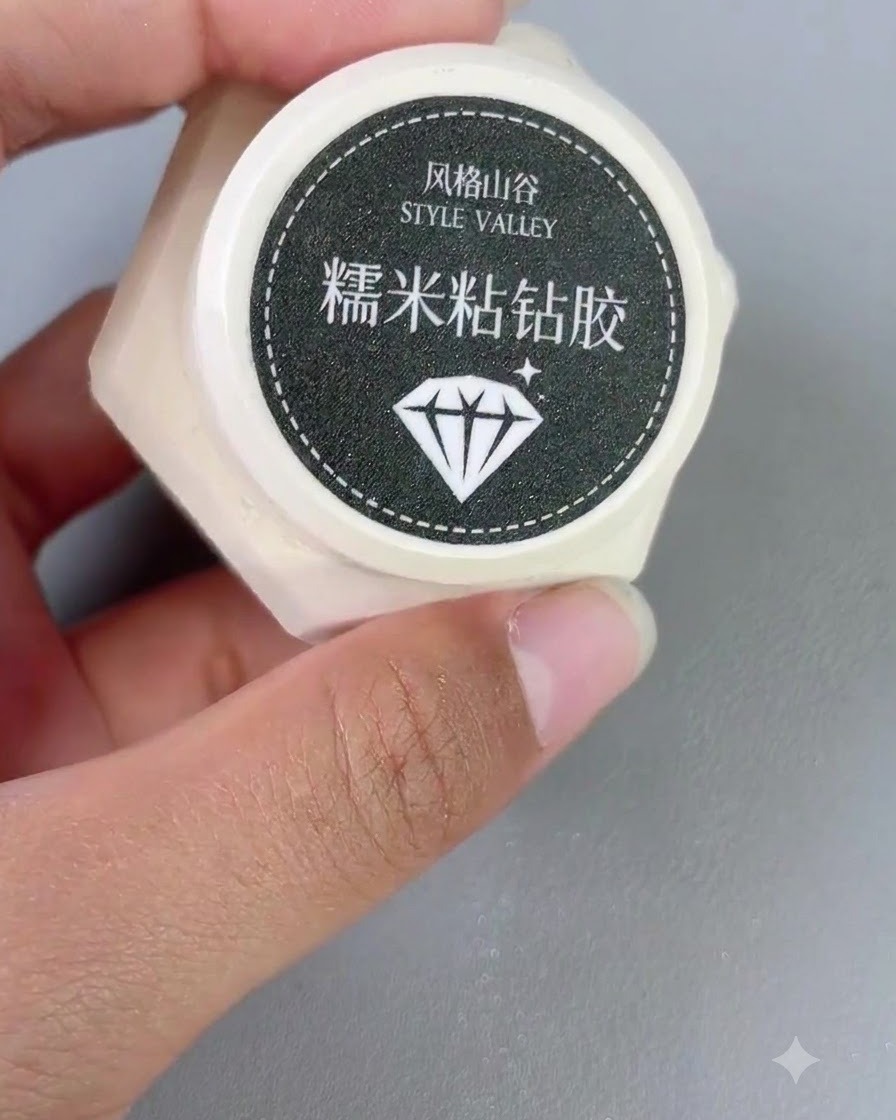 Ein kleiner Behälter mit Style Valley Sticky Diamond Gel wird neben einem Nagelpinsel in einer Hand gehalten.