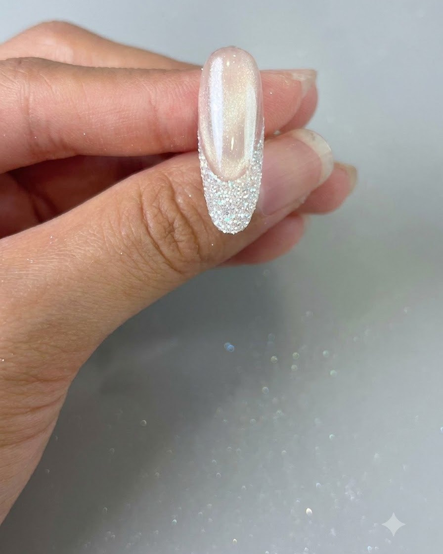 Eine Hand hält einen fertigen Nagel mit einer Glitzer-French-Spitze, bereit für die finale Aushärtung.