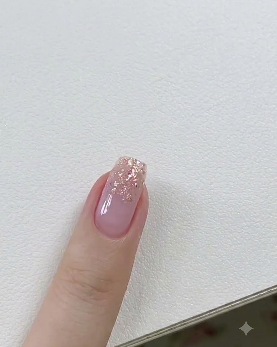 Ein Gelpinsel trägt eine dünne Schicht klares Builder-Gel auf einen mit Glitzer akzentuierten Fingernagel auf.
