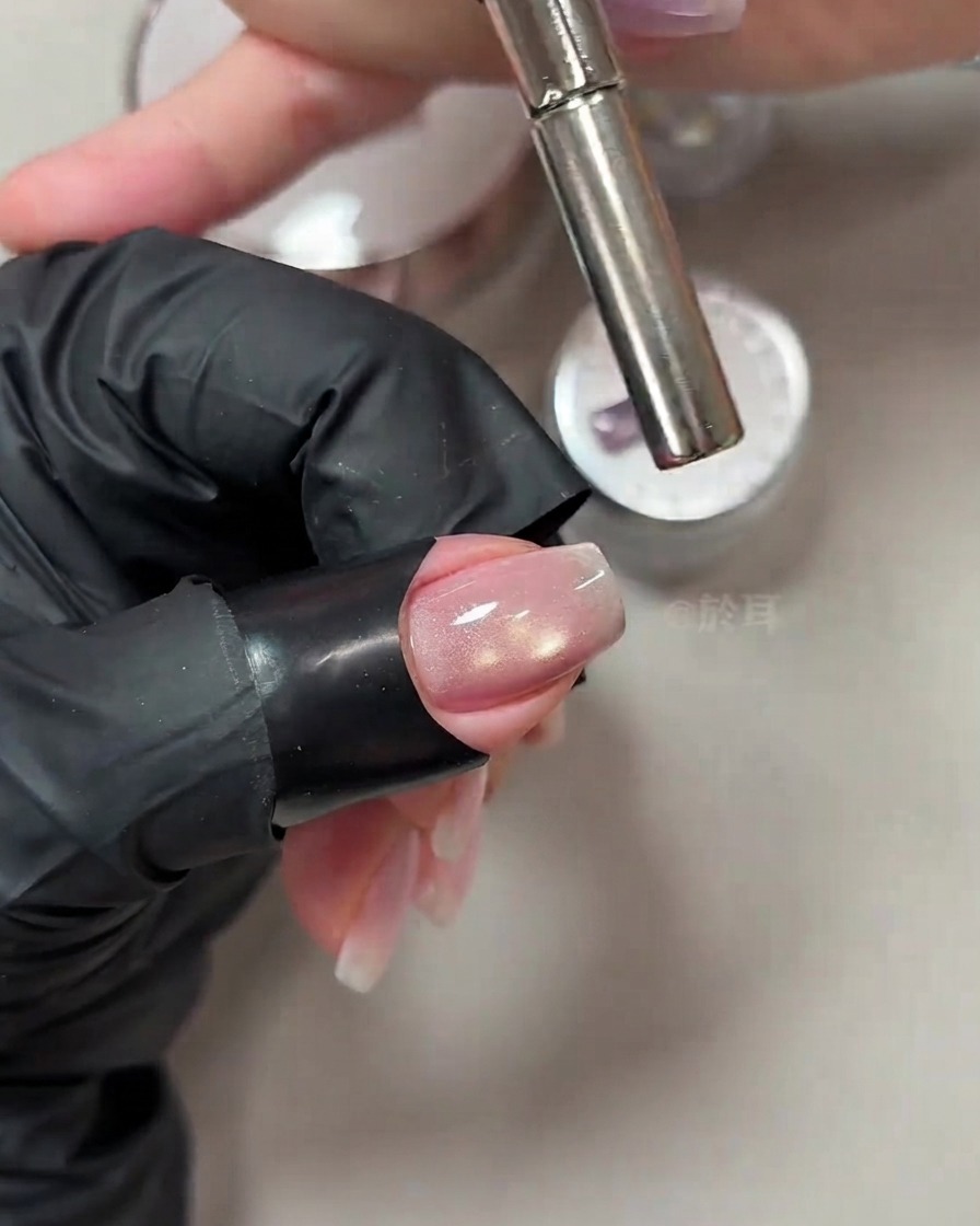 Ein zylindrischer Magnetstab wird nah an die Spitze eines manikürten Nagels gehalten, um den Cat-Eye-Schimmer zu lenken.