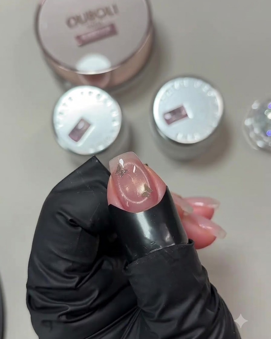 Nahaufnahme eines Fingers mit einer Schmetterlings-Paillette, die unter einer kleinen weißen tragbaren UV-Lampe ausgehärtet wird.