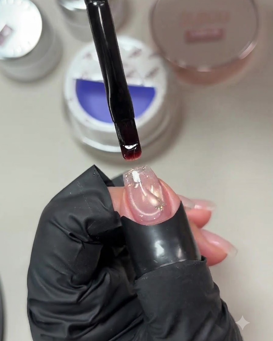 Ein Pinsel hält einen Tropfen zartviolett-blaues Builder-Gel über einem vorbereiteten Nagel mit einer eingebetteten Paillette.