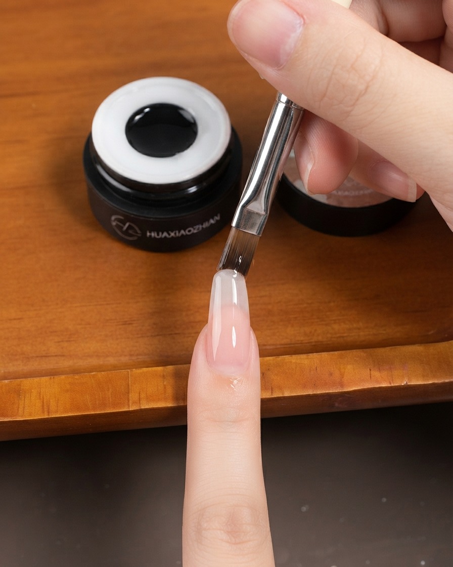 Ein flacher Gelpinsel trägt eine dünne Gelschicht auf einen langen mandelförmigen Fingernagel auf.